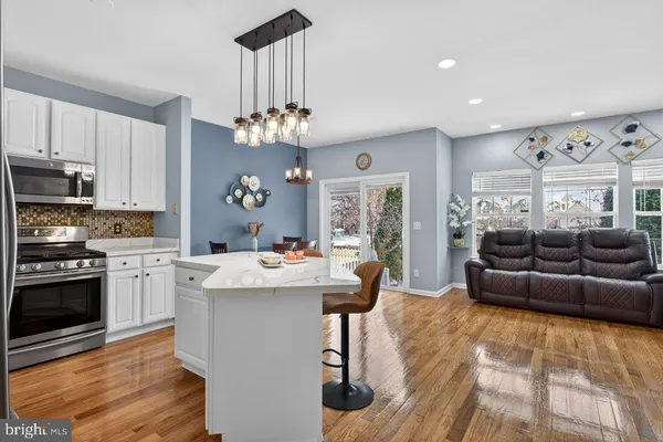 a living room with stainless steel appliances furniture a chandelier and a kitchen view
