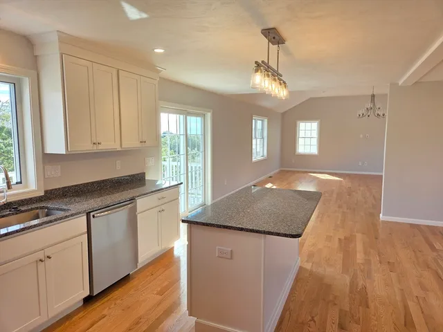 a kitchen with granite countertop a stove a sink dishwasher and white cabinets with wooden floor