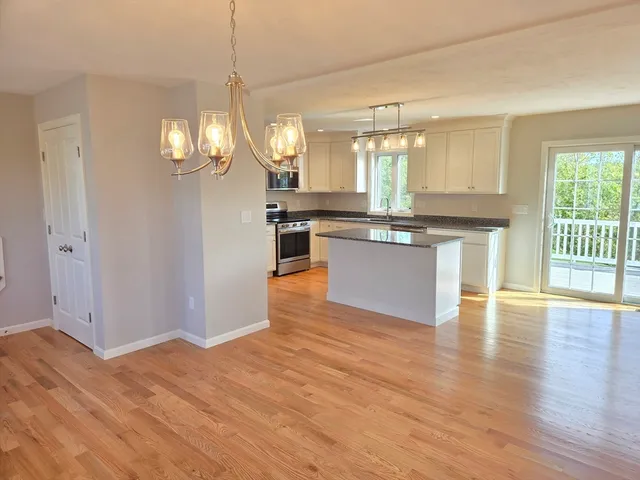 a large kitchen with granite countertop a stove top oven a sink dishwasher and white cabinets with wooden floor