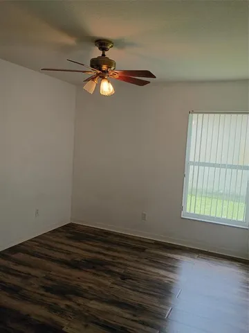 an empty room with wooden floor fan and windows