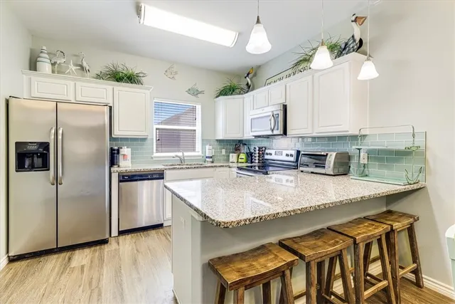 a kitchen with stainless steel appliances granite countertop a sink a stove a refrigerator cabinets and a dining table with wooden floor