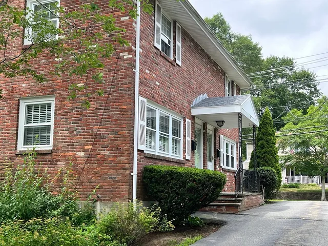 a view of a brick house with a yard and large trees