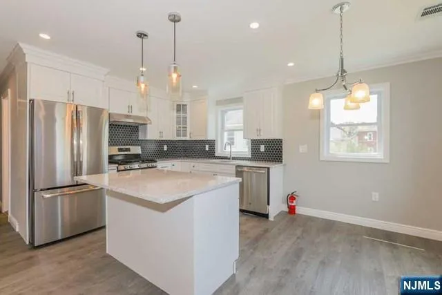 a kitchen with stainless steel appliances granite countertop a refrigerator a sink dishwasher a stove and white cabinets with wooden floor