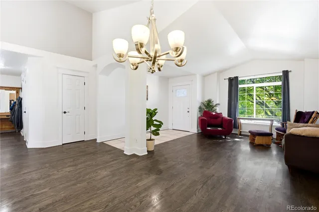a living room with couches chandelier and a dining table with wooden floor