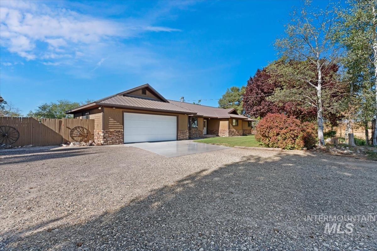 8275 Washoe Road Fruitland, ID 83619 - Photo 37 of 43 Wood-sided exterior with stone accents, attached garage with white door, gravel driveway, and mature landscaping