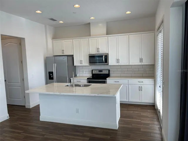 a large kitchen with stainless steel appliances granite countertop a stove a refrigerator a sink and white cabinets with wooden floor