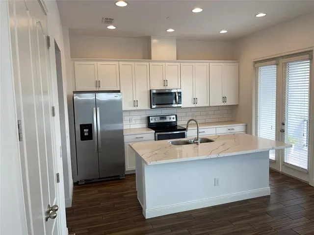 a large kitchen with stainless steel appliances granite countertop a stove a refrigerator and a sink with wooden floor