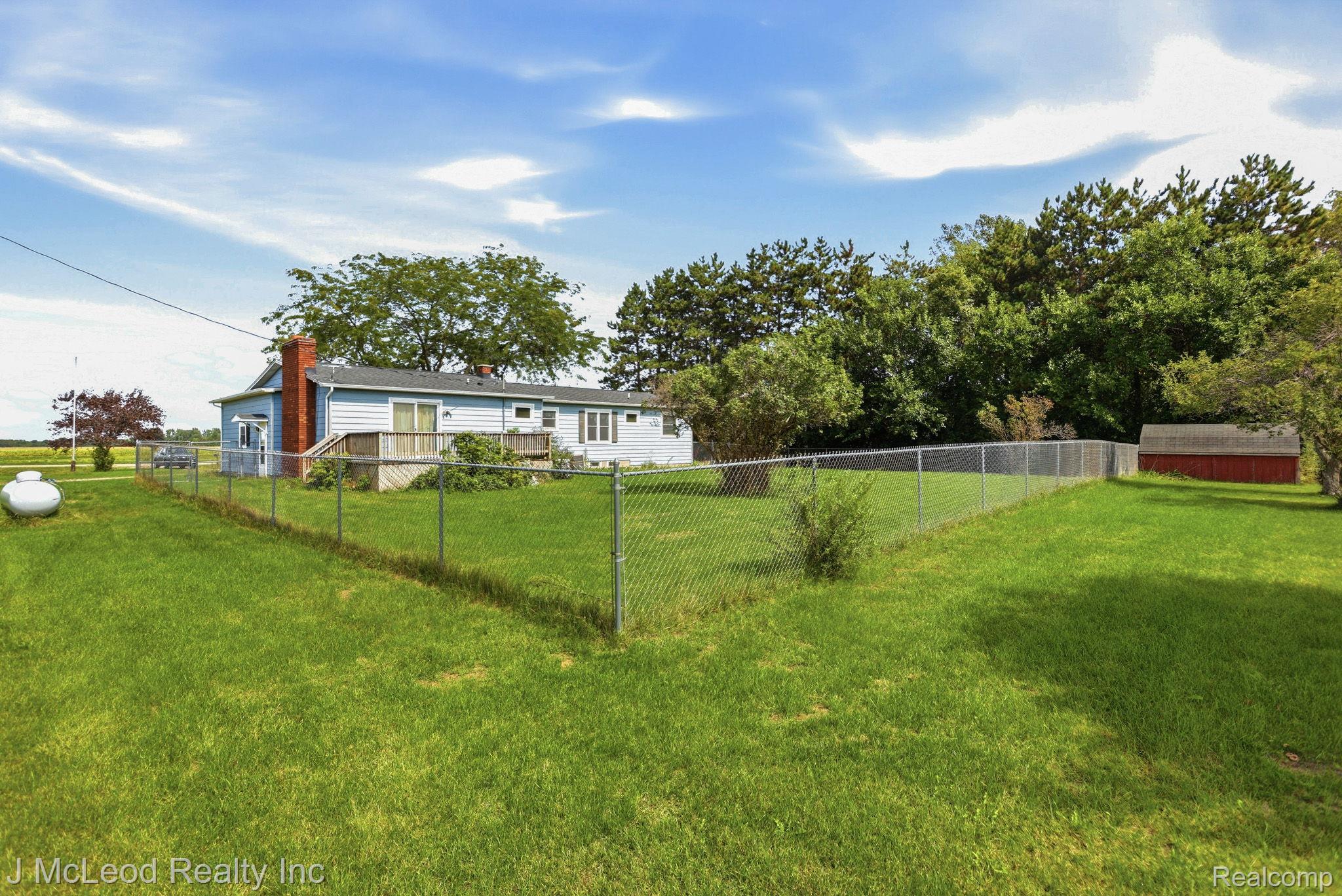 9481 Swaffer Road Vassar, MI 48768 - Photo 36 of 39 Expansive grassy area with chain-link fencing, mature trees, and a detached red shed
