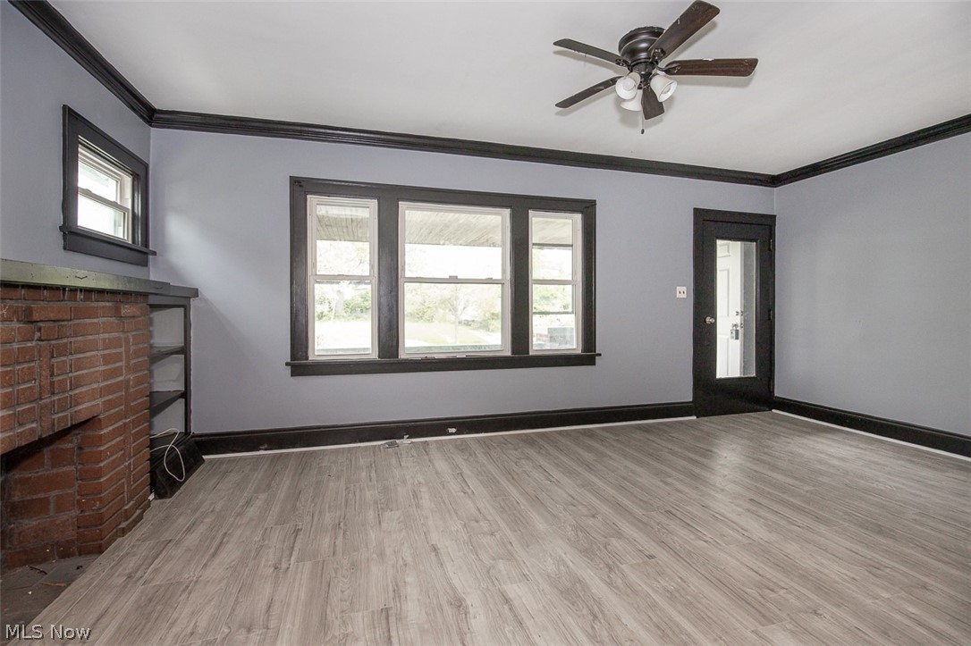1868-1870 Lampson Road Cleveland, OH 44112 - Photo 22 of 36 Spacious room featuring wood-finish flooring, a brick fireplace with built-in shelving, multiple windows, a ceiling fan with integrated lighting, and a glass-paneled door