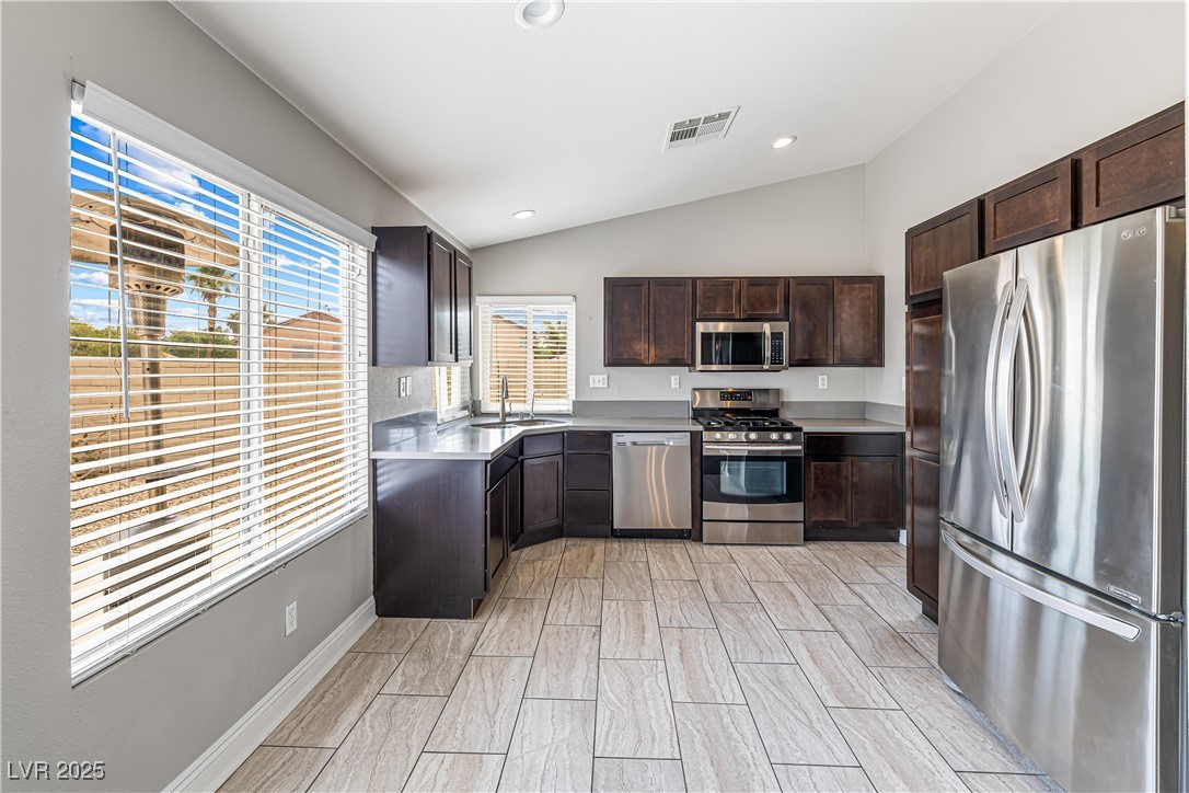 Kitchen with appliances with stainless steel finishes, light countertops, dark brown cabinetry, lofted ceiling, and wood finish floors
