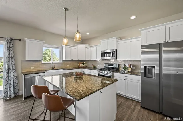 a kitchen with granite countertop kitchen island stainless steel appliances a table chairs refrigerator and microwave