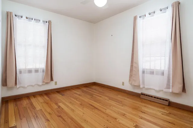 an empty room with wooden floor closet and windows