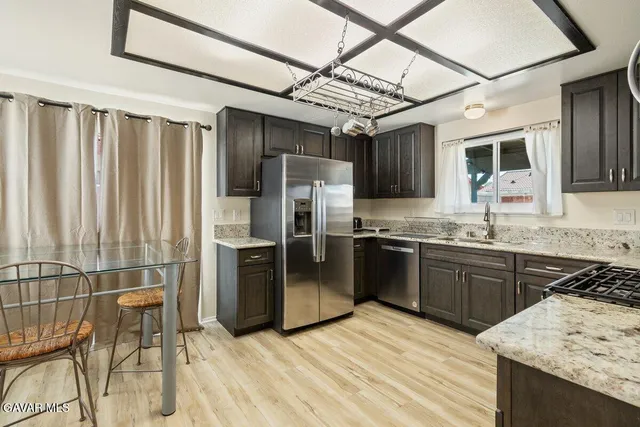 a kitchen with stainless steel appliances granite countertop a refrigerator a sink dishwasher a stove and white cabinets with wooden floor