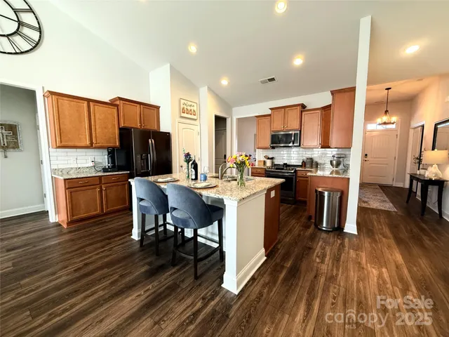 a kitchen with stainless steel appliances a refrigerator a stove a sink dishwasher a dining table and chairs with wooden floor