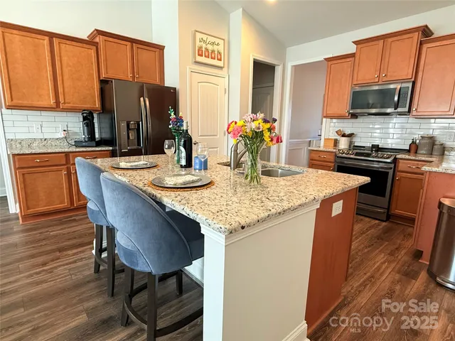 a kitchen with stainless steel appliances granite countertop a kitchen island a stove a refrigerator a sink a dining table and chairs with wooden floor