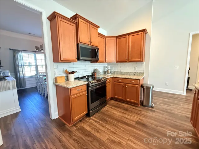 a kitchen with stainless steel appliances granite countertop a stove top oven a sink dishwasher a microwave oven and a dining table with wooden floor