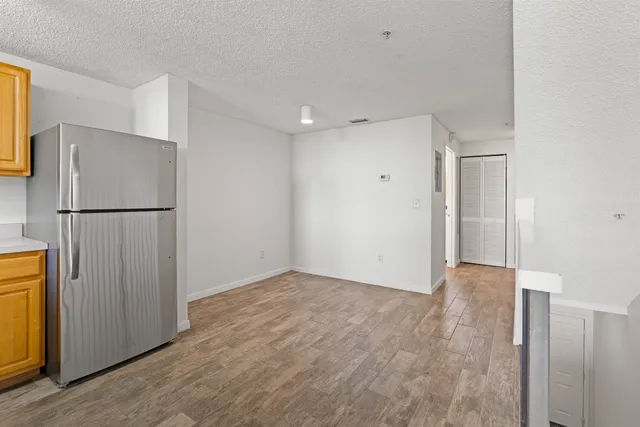 a view of an empty room with wooden floor and a refrigerator