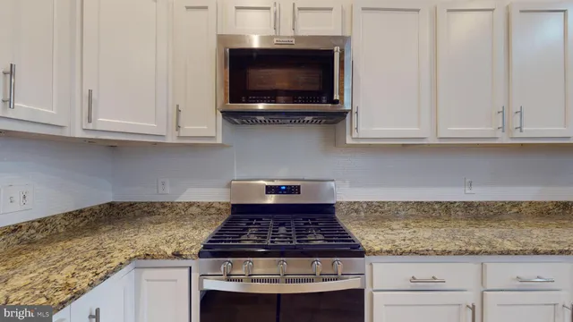 a kitchen with granite countertop a stove and a white cabinets
