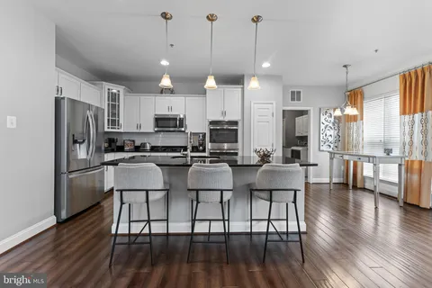 a kitchen with stainless steel appliances kitchen island granite countertop a refrigerator a stove a island a dining table and chairs with wooden floor