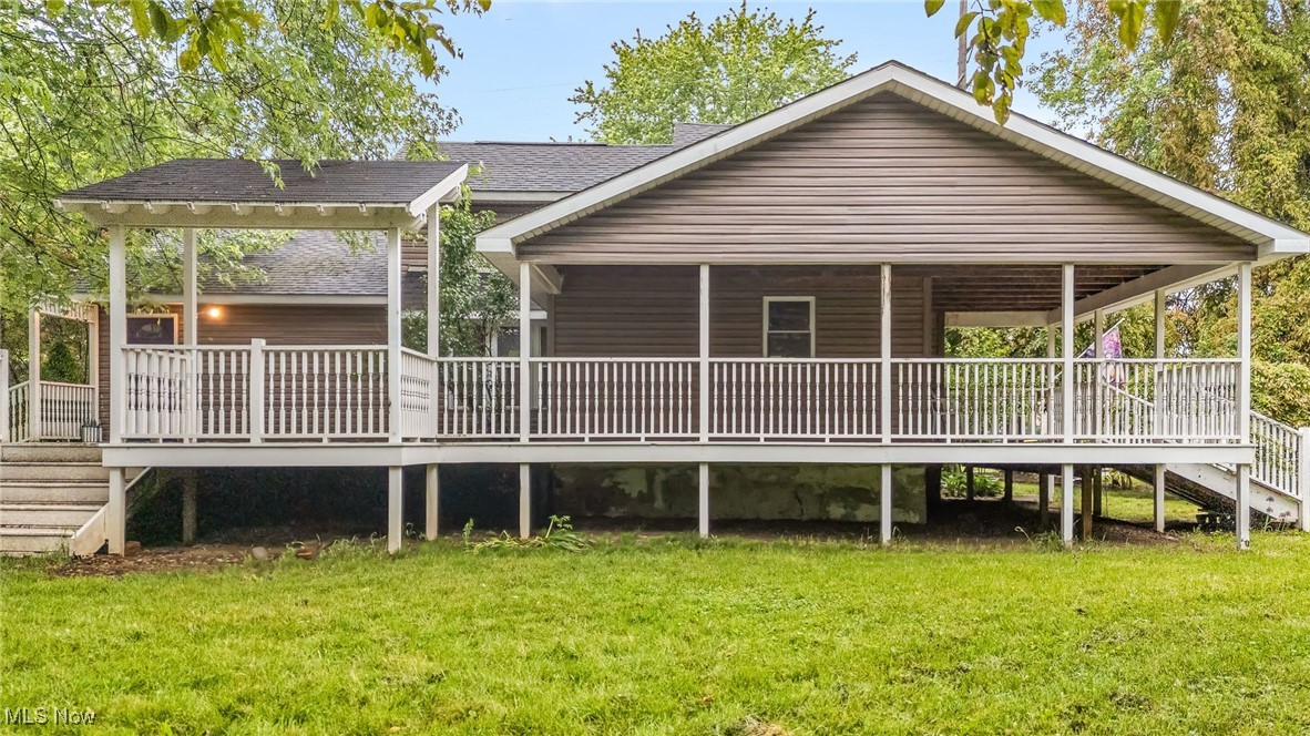 Front view of property featuring a yard, stairs, roof with shingles, and a wooden deck