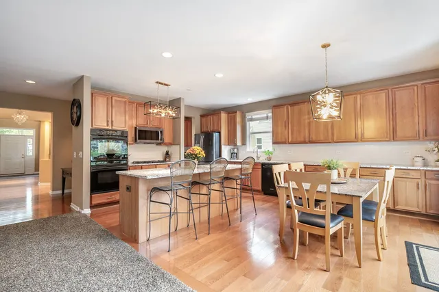 a kitchen with stainless steel appliances granite countertop a stove a refrigerator a kitchen island a dining table and chairs with wooden floor