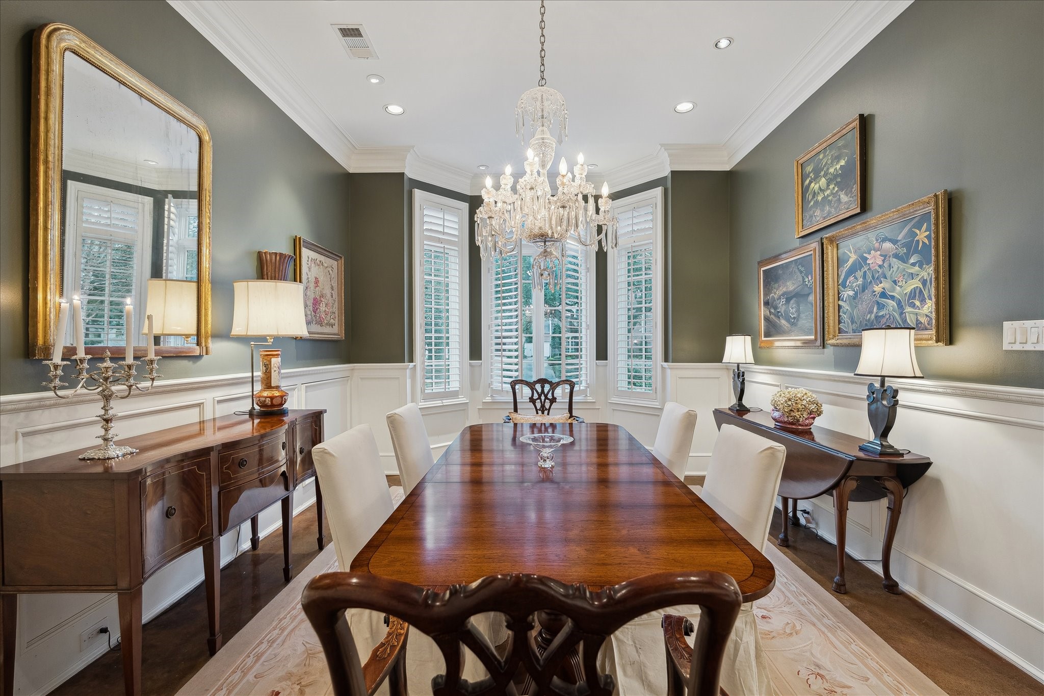 3109 Locke Lane Houston, TX 77019 - Photo 21 of 50 Designed for both intimate dinners and formal gatherings, the dining room showcases rich hardwood floors and elegant millwork throughout. A statement chandelier anchors the space beneath detailed crown molding, with a bay window and plantation shutters adding charm and soft, filtered light.