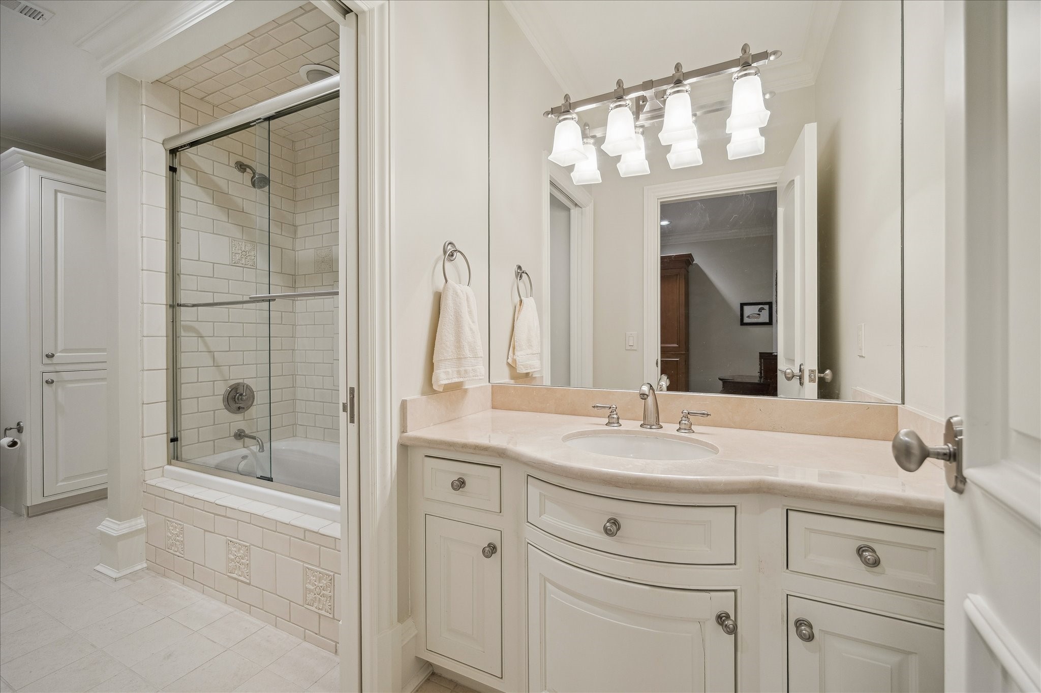 3109 Locke Lane Houston, TX 77019 - Photo 33 of 50 This thoughtfully designed guest bathroom is shared between Bedroom 1 and Bedroom 2, with each bedroom enjoying its own private vanity area with undermount sinks and custom cabinetry. A pocket door separates the vanities from the shared tub/shower combination with tiled surround, built-in shower niche, and brushed nickel fixtures, blending privacy and convenience.