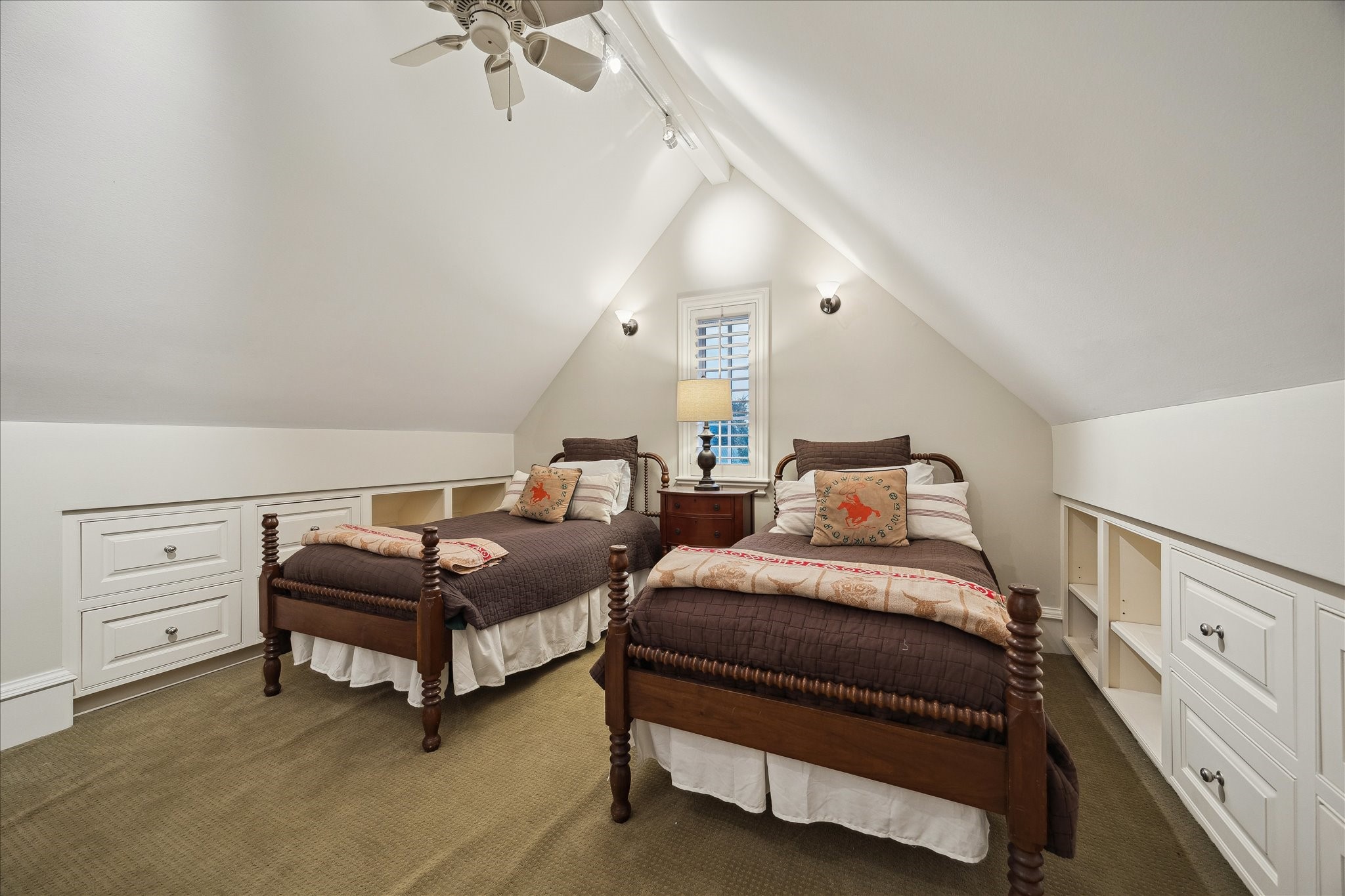 3109 Locke Lane Houston, TX 77019 - Photo 36 of 50 Guest Bedroom No. 3 on the third floor is a spacious retreat with a vaulted ceiling, ceiling fan, and plush carpeted floors. Three windows with plantation shutters fill the room with natural light, while built-in shelving and dresser drawers, a seating area, in-ceiling speakers, and track and recessed lighting enhance both function and comfort. A walk-in closet with built-in drawers completes this thoughtfully designed space.