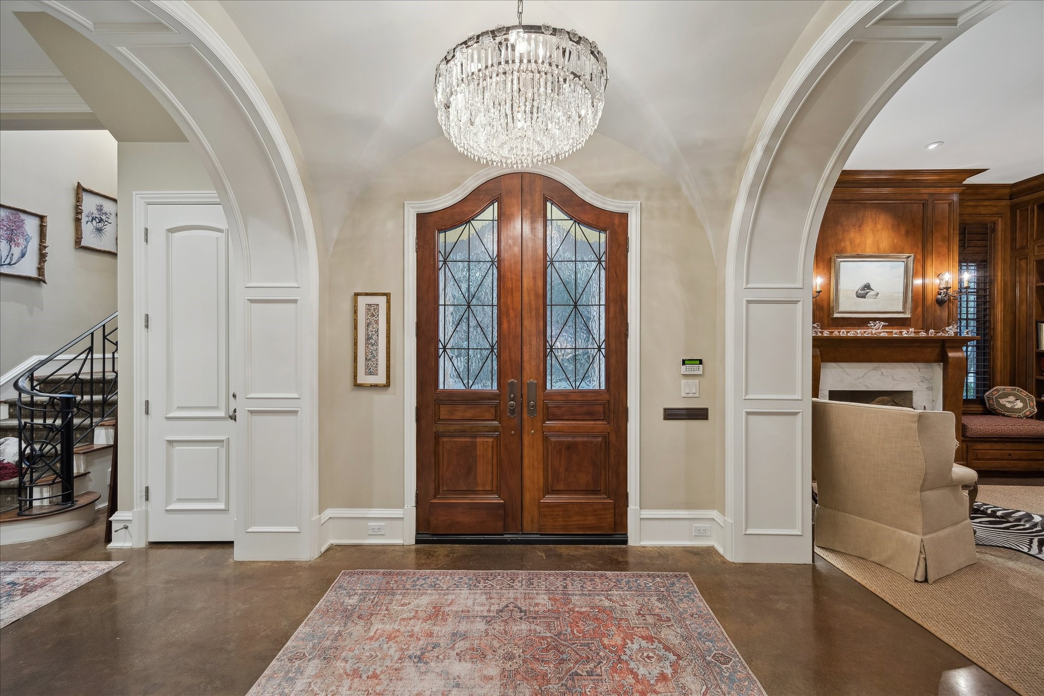 3109 Locke Lane Houston, TX 77019 - Photo 4 of 50 Step inside to a stunning groin-vaulted foyer, where a statement chandelier sets the tone for the elegance that unfolds beyond. Neutral designer wallpaper and stained concrete floors create a warm yet refined first impression, while beautifully encased openings frame the spaces ahead with architectural distinction.