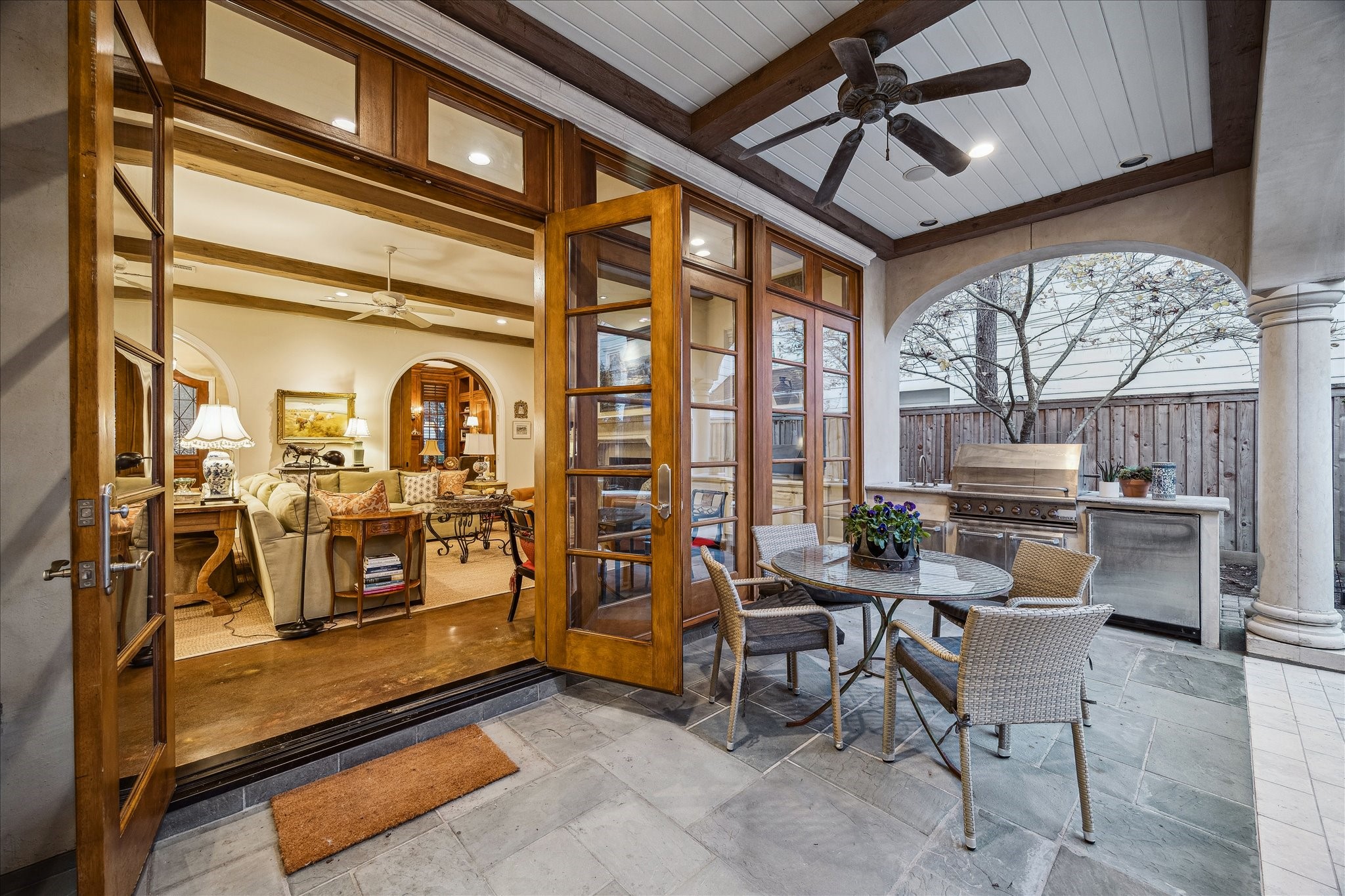 3109 Locke Lane Houston, TX 77019 - Photo 45 of 50 The covered patio and summer kitchen offer a perfect blend of indoor-outdoor living, featuring natural stone flooring, a ceiling fan, and a shaded seating area. An outdoor kitchen and grilling space provide effortless entertaining, with direct access from the family room through wood-framed French doors.