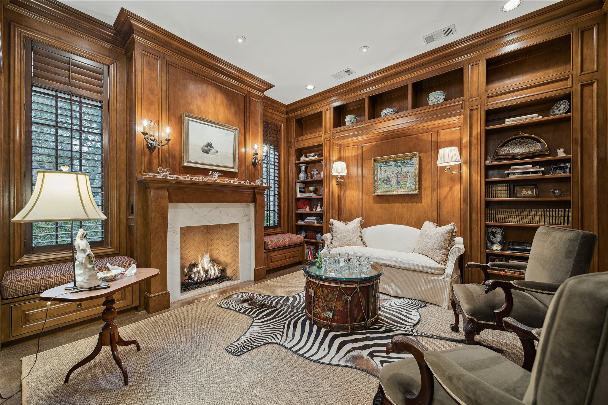 3109 Locke Lane Houston, TX 77019 - Photo 6 of 50 Through an elegant arched entry, this stately library blends timeless craftsmanship with modern amenities. Custom built-ins, crown molding, and detailed wall paneling complement the stone fireplace, while recessed lighting, decorative sconces, and in-ceiling speakers enhance the ambiance—perfectly illuminated by windows that fill the space with natural light.