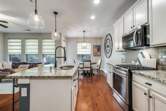 a kitchen with stainless steel appliances granite countertop a stove a sink dishwasher a dining table and chairs with wooden floor