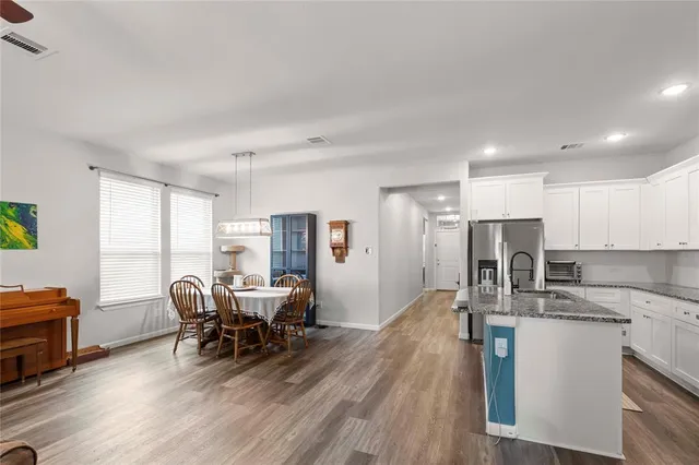 a kitchen with stainless steel appliances granite countertop a stove top oven a sink dishwasher a dining table and chairs with wooden floor