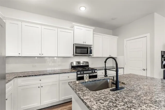 a kitchen with granite countertop a stove and white cabinets