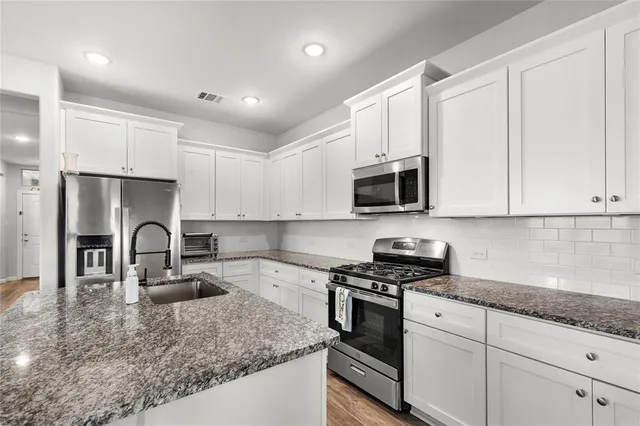 a kitchen with granite countertop a sink stainless steel appliances and white cabinets