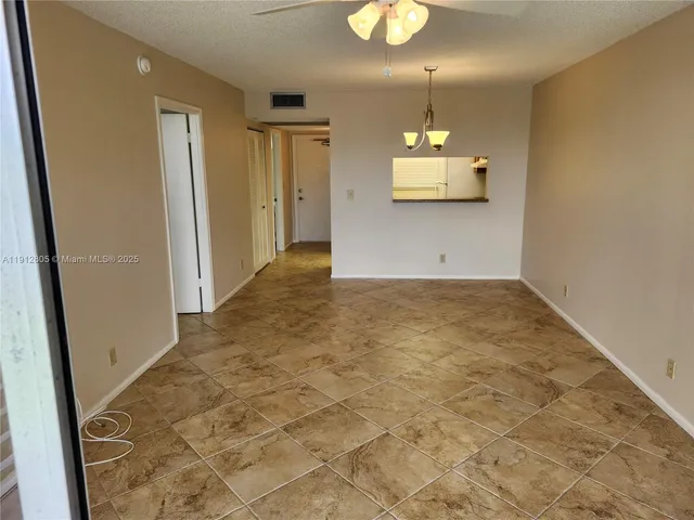 an empty room with kitchen and chandelier fan
