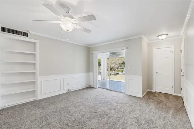 an empty room with a ceiling fan and kitchen view