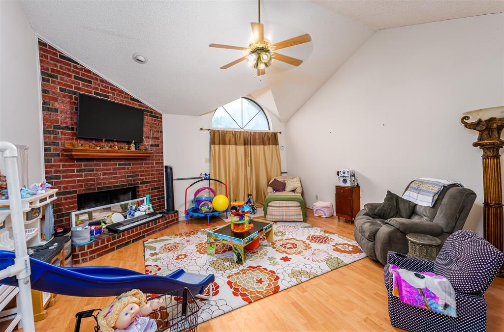 601 Houston School Road Red Oak, TX 75154 - Photo 10 of 32 Living area with vaulted ceiling, a ceiling fan, wood finished floors, a fireplace, and a textured ceiling