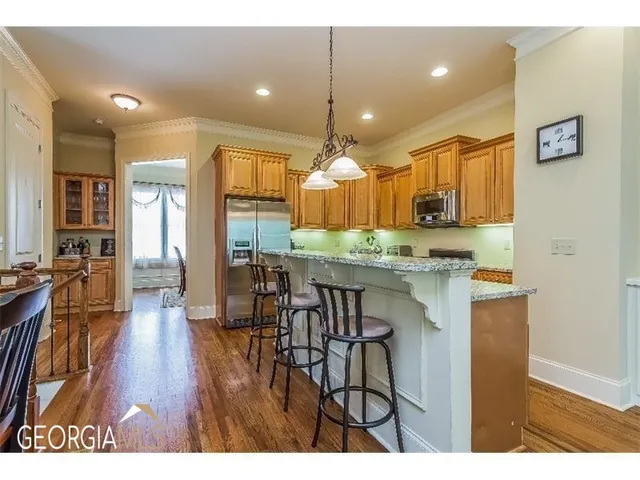 a kitchen with stainless steel appliances kitchen island granite countertop a stove a refrigerator a sink a dining table and chairs with wooden floor
