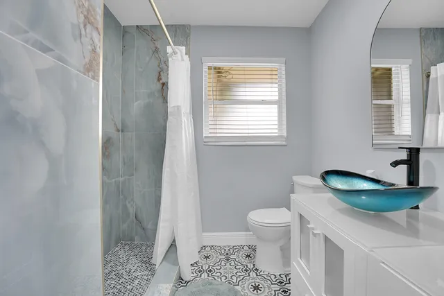 a bathroom with a granite countertop sink a toilet a mirror and shower
