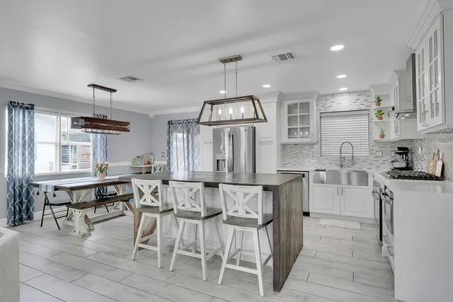 a kitchen with stainless steel appliances kitchen island granite countertop a table chairs refrigerator and cabinets