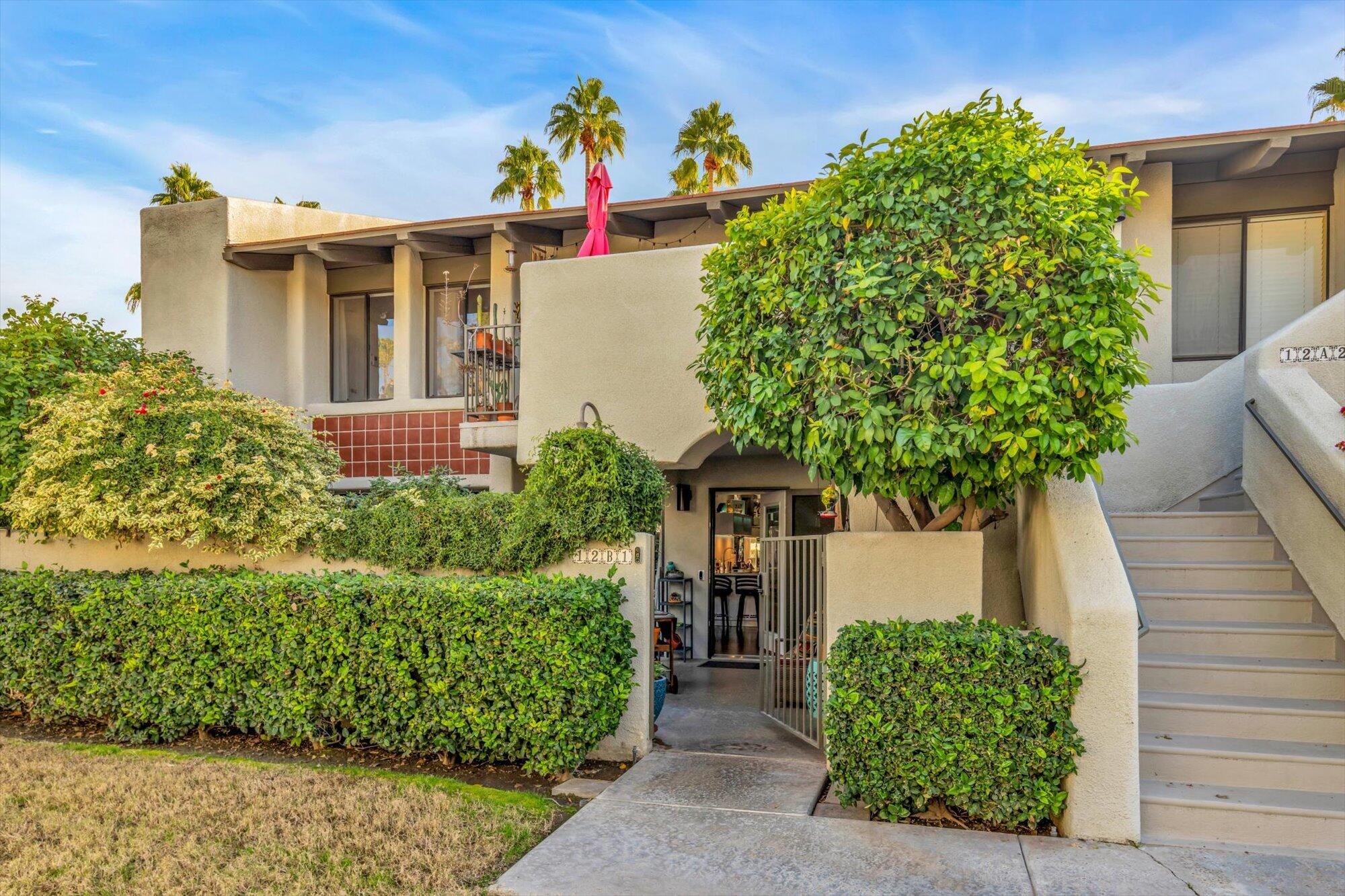 1100 East Amado Road, Unit 12B1 Palm Springs, CA 92262 - Photo 25 of 29 a front view of a house with a yard and potted plants
