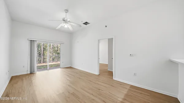 an empty room with wooden floor chandelier fan and windows