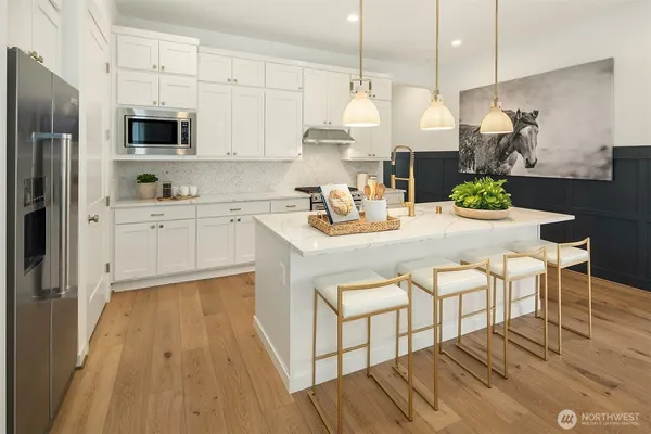 a kitchen with stainless steel appliances a stove a sink a microwave a refrigerator and white cabinets with wooden floor