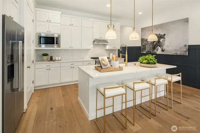 a kitchen with stainless steel appliances a stove a sink a microwave a refrigerator and white cabinets with wooden floor