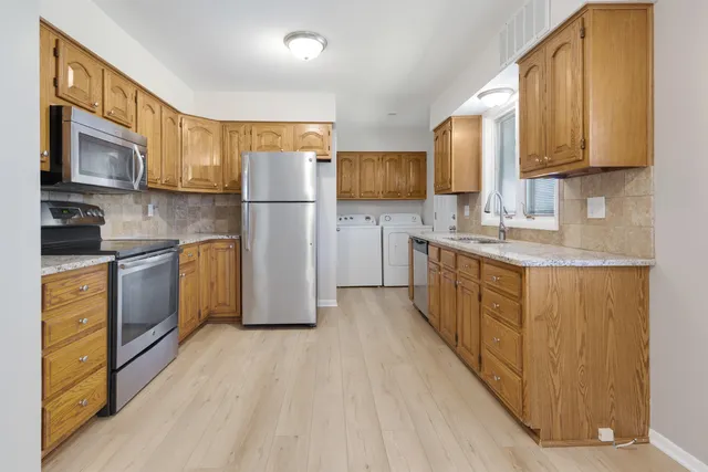 a kitchen with stainless steel appliances granite countertop a refrigerator a stove top oven a sink dishwasher and wooden cabinets with wooden floor