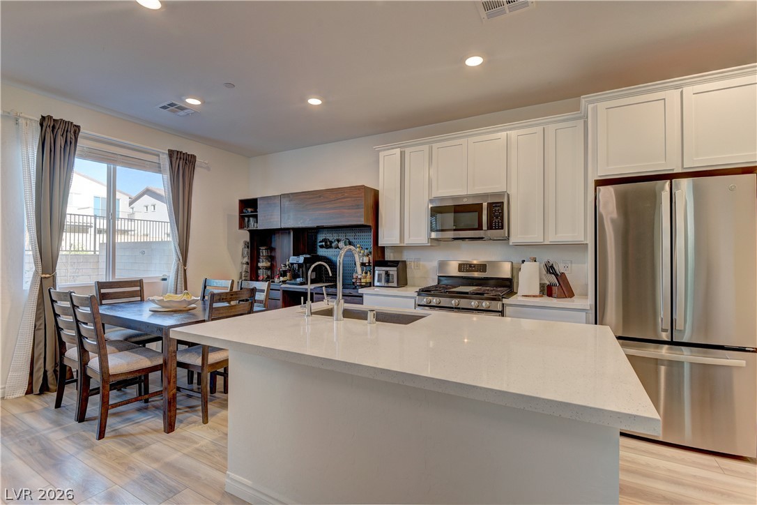 8827 Roadrunner Ravine Street Las Vegas, NV 89166 - Photo 13 of 17 Kitchen with stainless steel appliances, white cabinets, a kitchen island with sink, light stone countertops, and recessed lighting