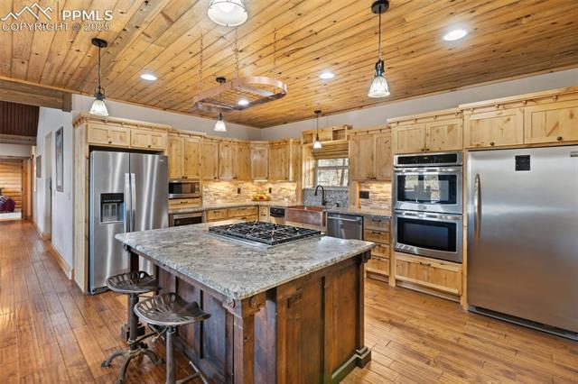 111 Blue Spruce Road Divide, CO 80814 - Photo 17 of 46 Kitchen with stainless steel appliances, light wood-type flooring, decorative backsplash, a center island, and light brown cabinets