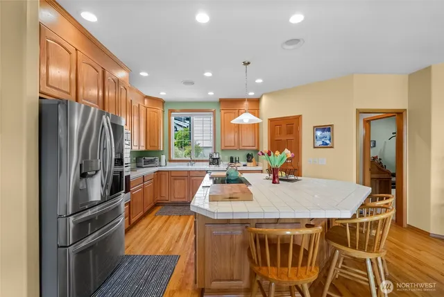 a kitchen with stainless steel appliances granite countertop a refrigerator a stove a sink dishwasher a dining table and chairs with wooden floor
