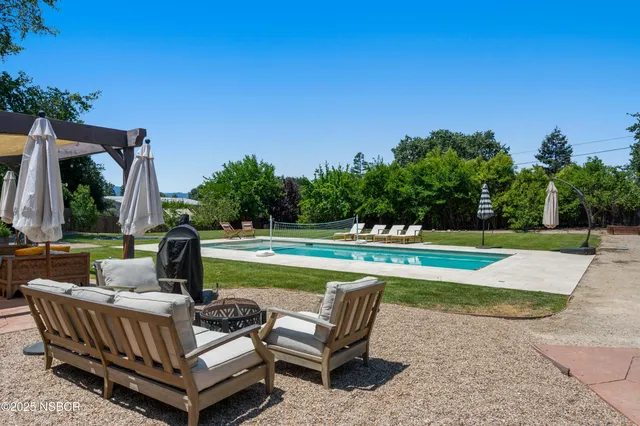 a view of swimming pool with seating space and trees in the background
